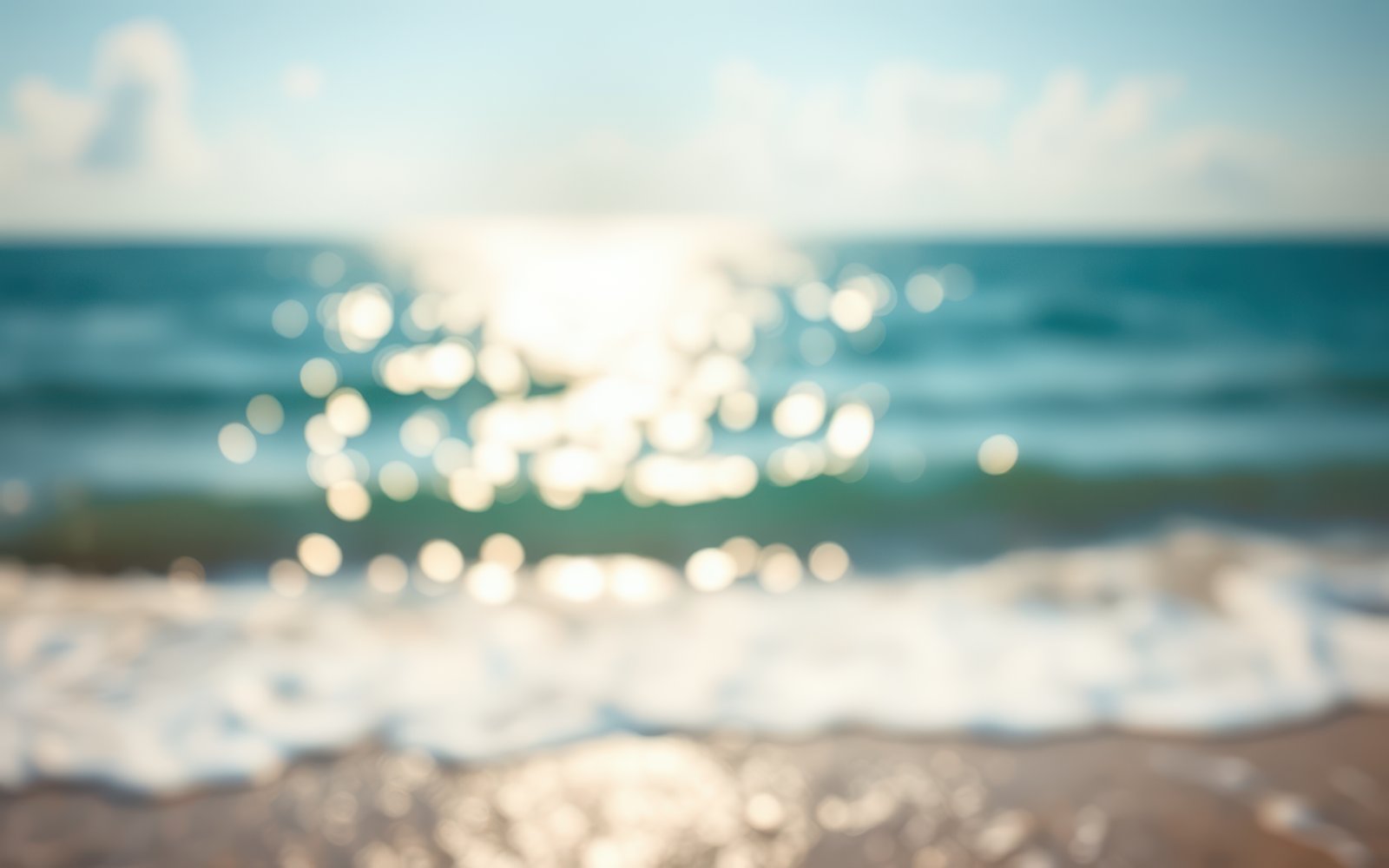 Bright sunlight reflecting on ocean waves at a sandy beach during the day